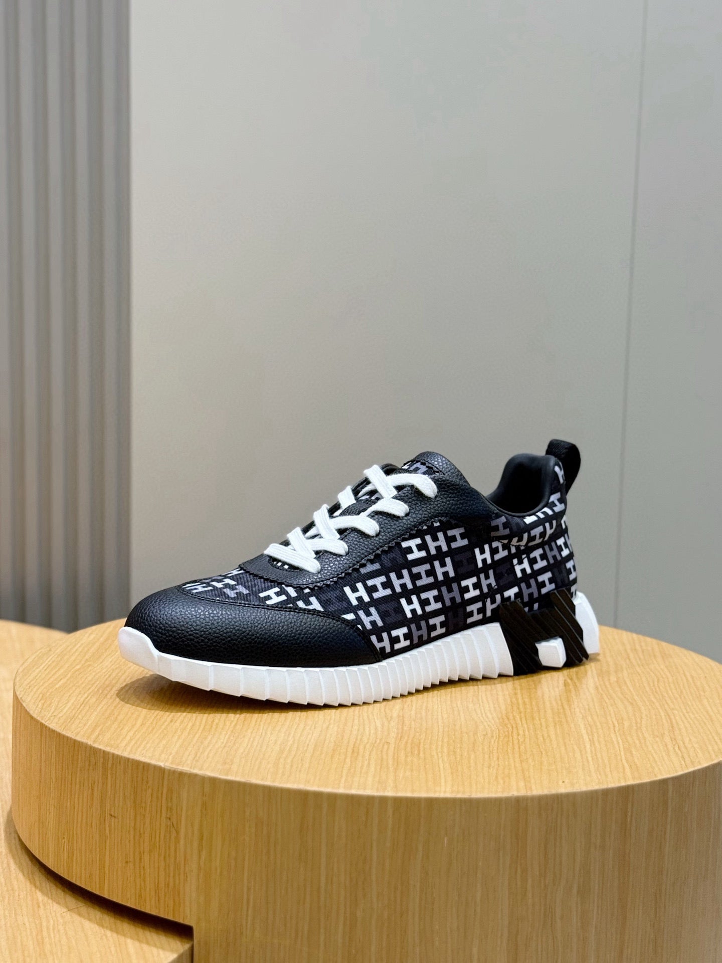 Black low-top sneaker with white laces, repeating H-style logo pattern, white sole