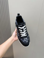 Black low-top sneaker in hand with white laces and repeating H-style logo pattern