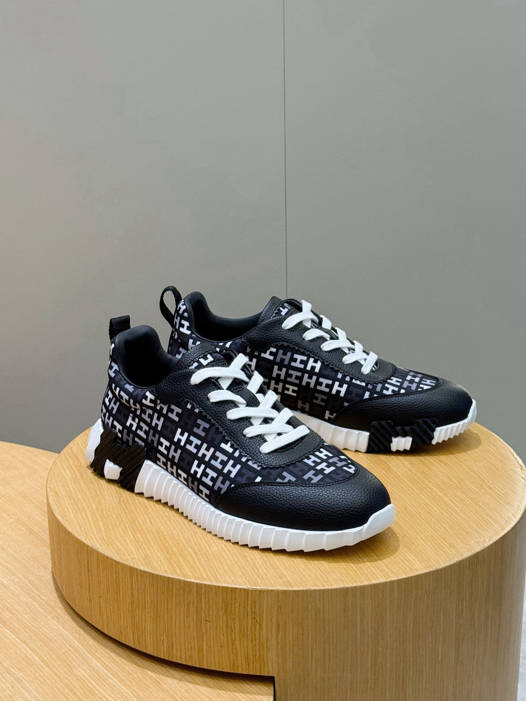 Pair of black low-top sneakers with white laces and repeating H-style logo pattern