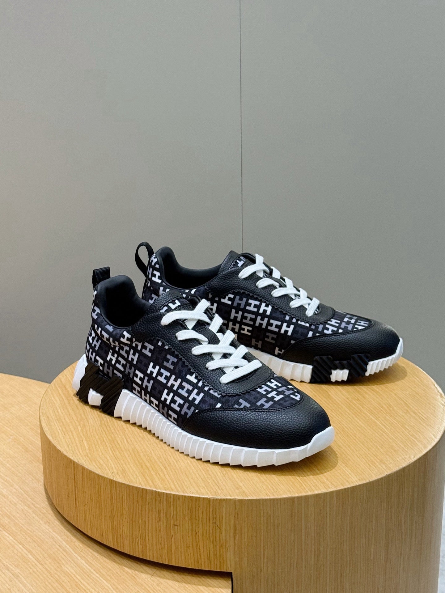 Pair of black low-top sneakers with white laces and repeating H-style logo pattern