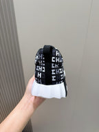 Black low-top sneaker heel view in hand with repeating H-style logo pattern