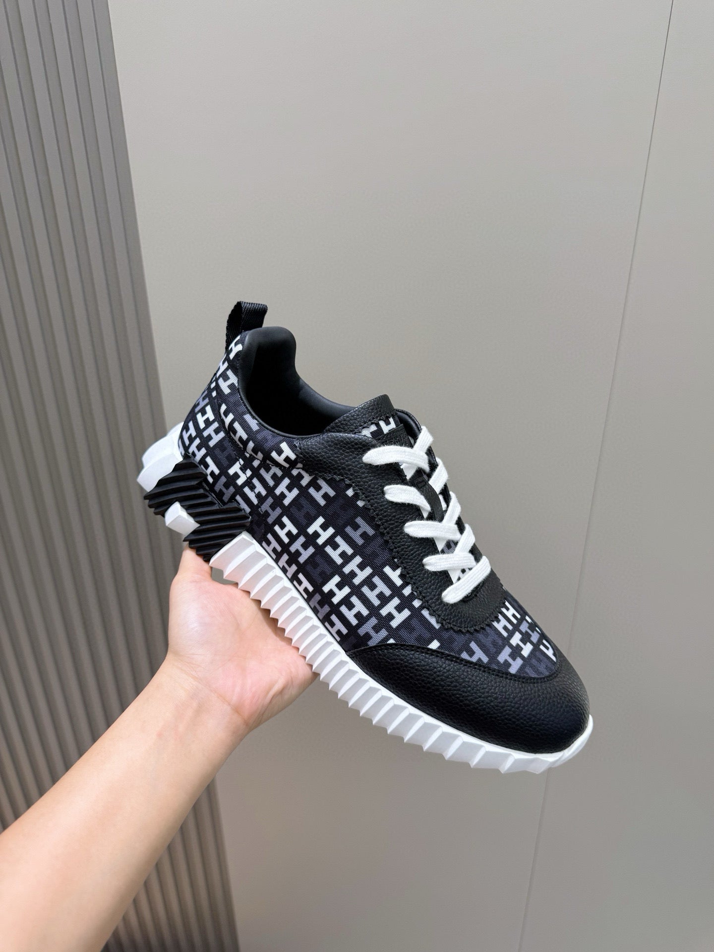 Black low-top sneaker angled view with white laces, repeating H-style logo pattern
