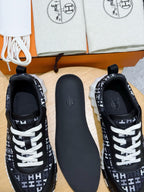 Black low-top sneakers with white laces and repeating H-style logo pattern, side view