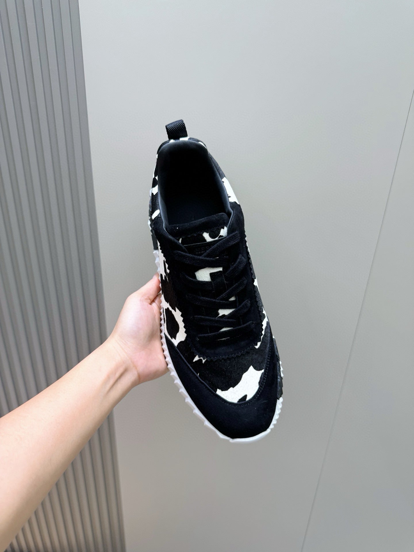 Unisex cow-print sneaker close-up, black laces, patterned side, white rubber sole.