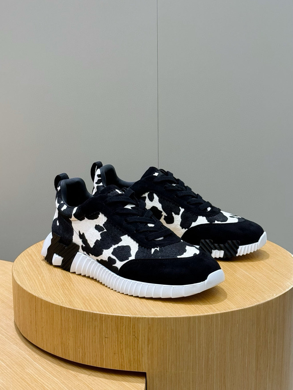 Unisex cow-print sneakers on display, black top with white pattern, white sole.