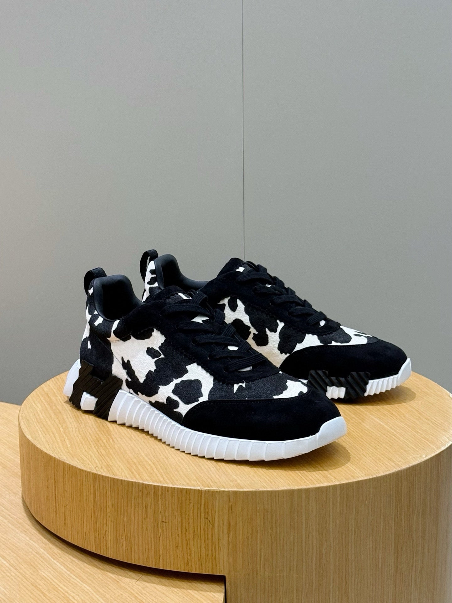 Unisex cow-print sneakers on display, black top with white pattern, white sole.