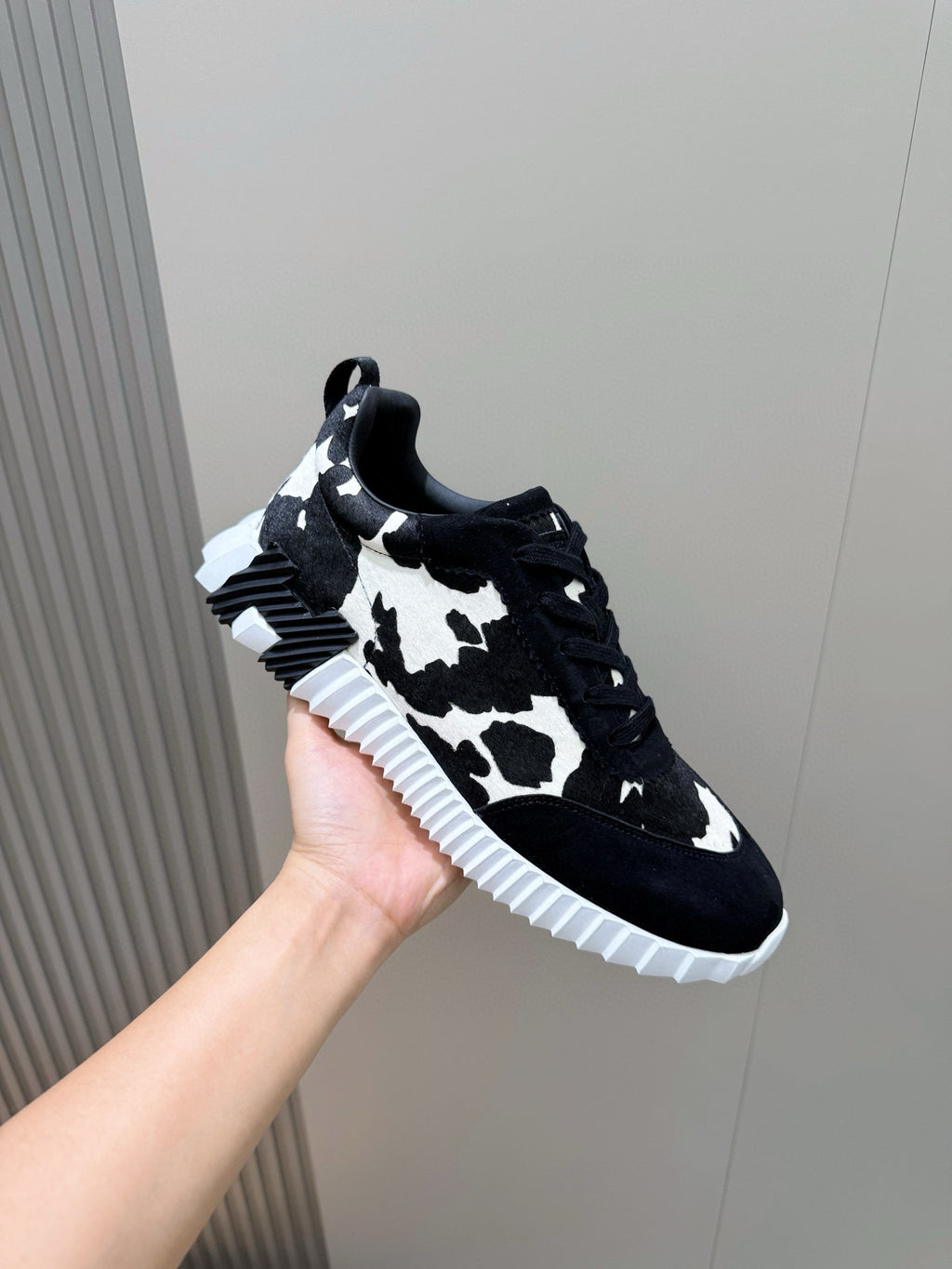 Unisex sneaker side view, black cow-print upper, lace-up with white rubber sole.