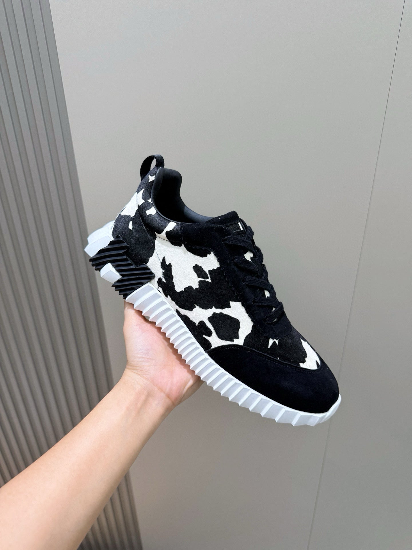 Unisex sneaker side view, black cow-print upper, lace-up with white rubber sole.