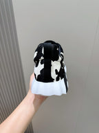 Unisex cow-print sneakers, heel view with black back tab, white midsole and sole.