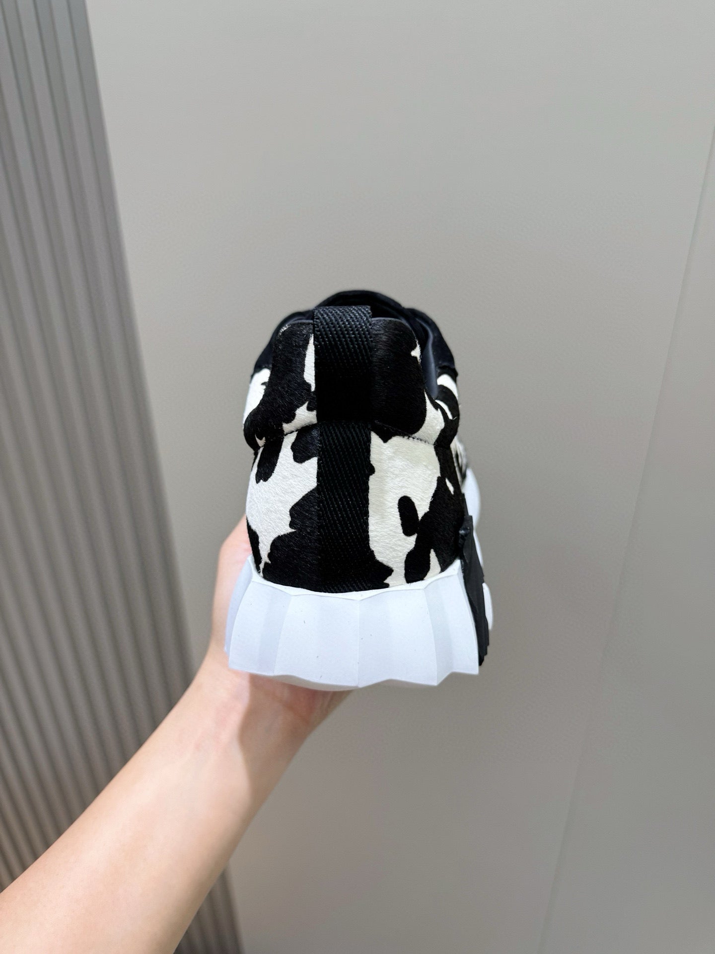 Unisex cow-print sneakers, heel view with black back tab, white midsole and sole.