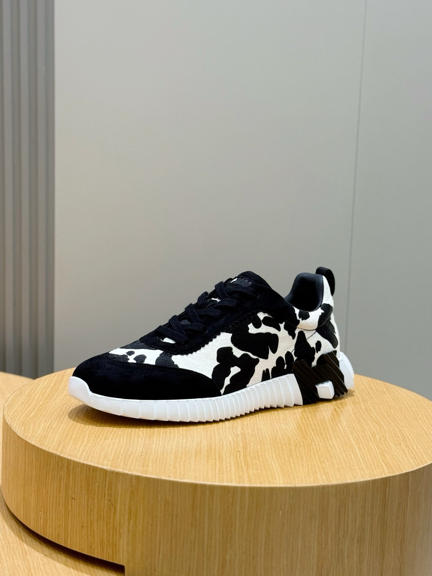 Cow-print unisex sneakers with black laces, low profile, white ridged sole.