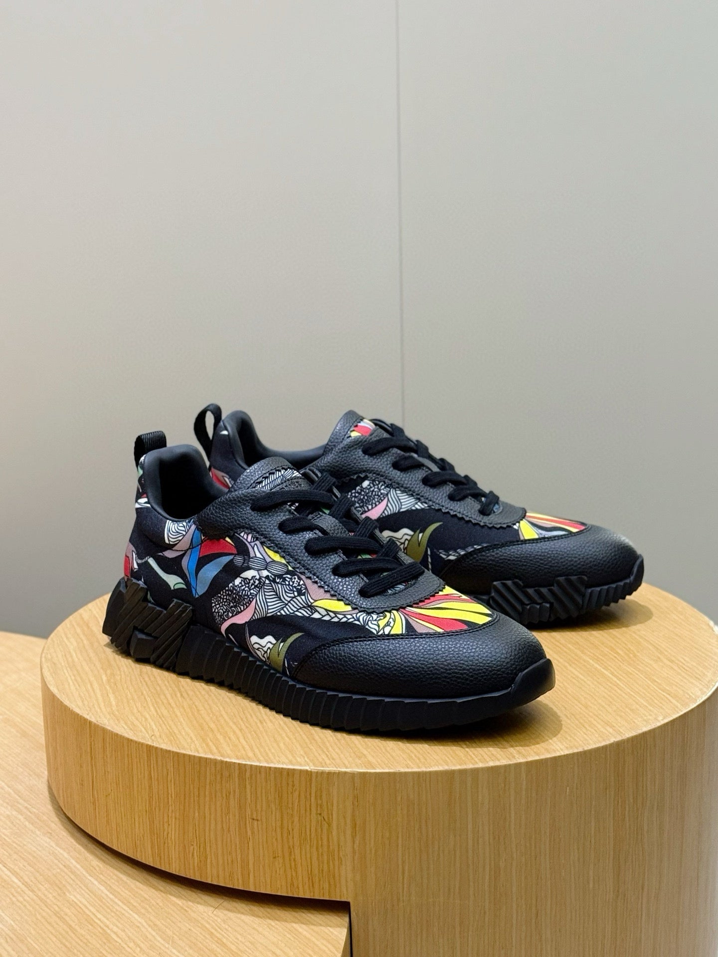 Black unisex lace-up sneakers with multicolor graphic panels and textured sole tread.