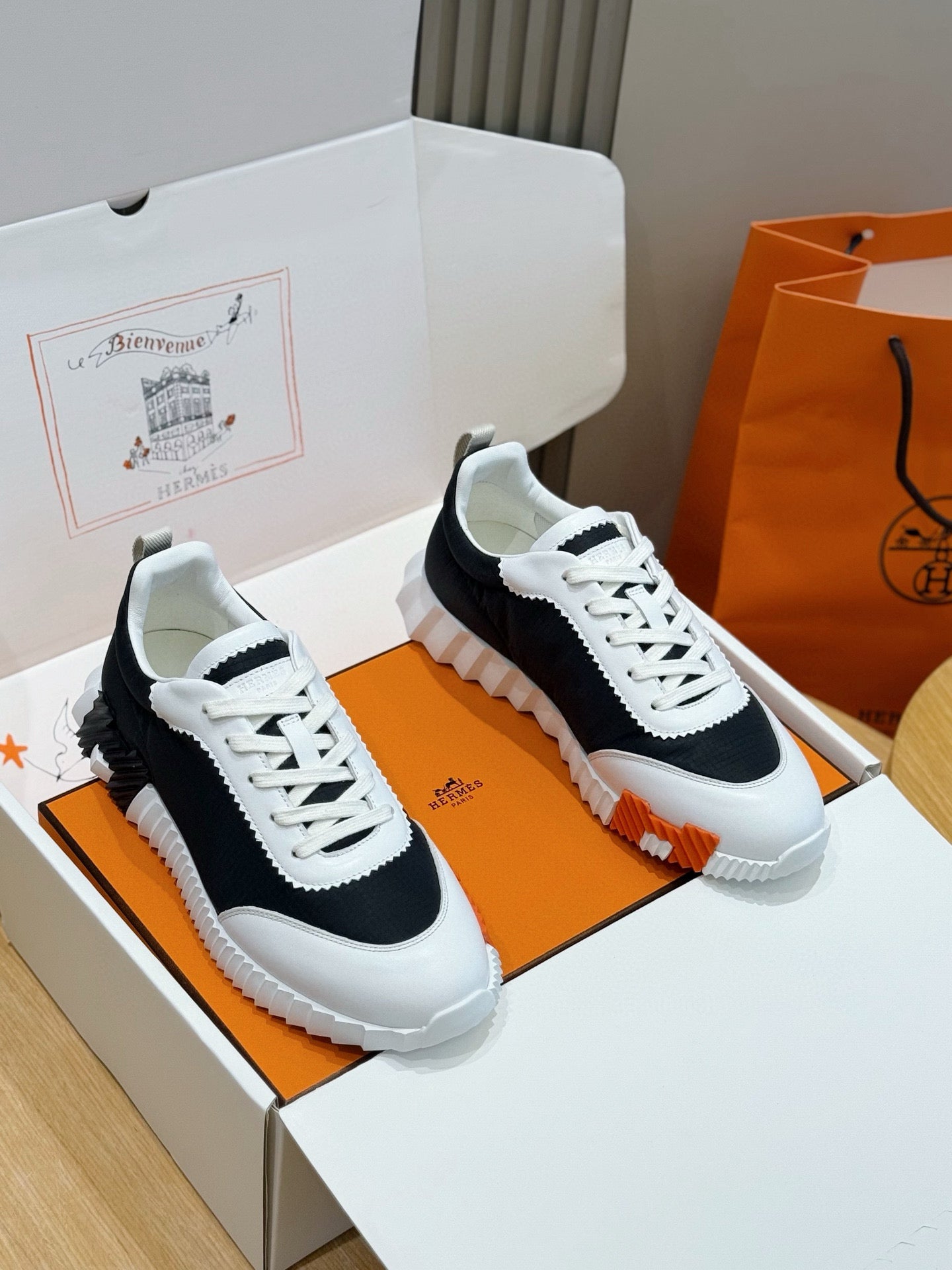 Hermes unisex sneakers, black and white with white laces and textured rubber sole.