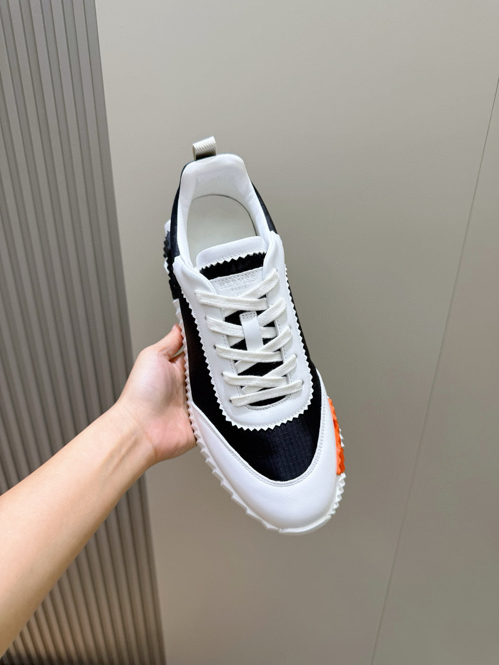 Hermes unisex sneakers held up by hand, black-and-white upper with white lace-up.