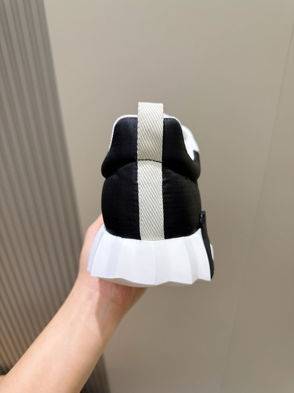 Hermes unisex sneakers heel view, black upper with white vertical stripe and sole.