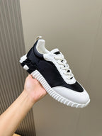 Hermes unisex sneakers, side view with black textile upper, white laces, ribbed sole.