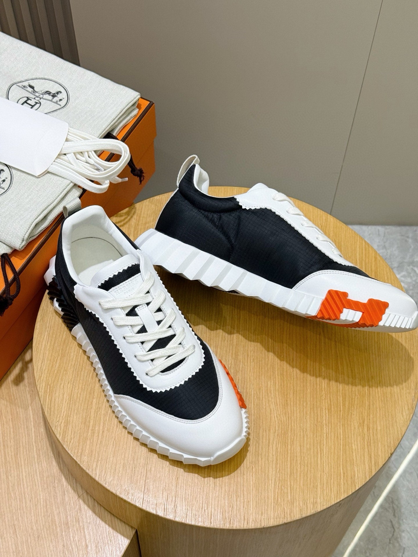 Hermes unisex sneakers pair on display, black-and-white with orange accent at the side.