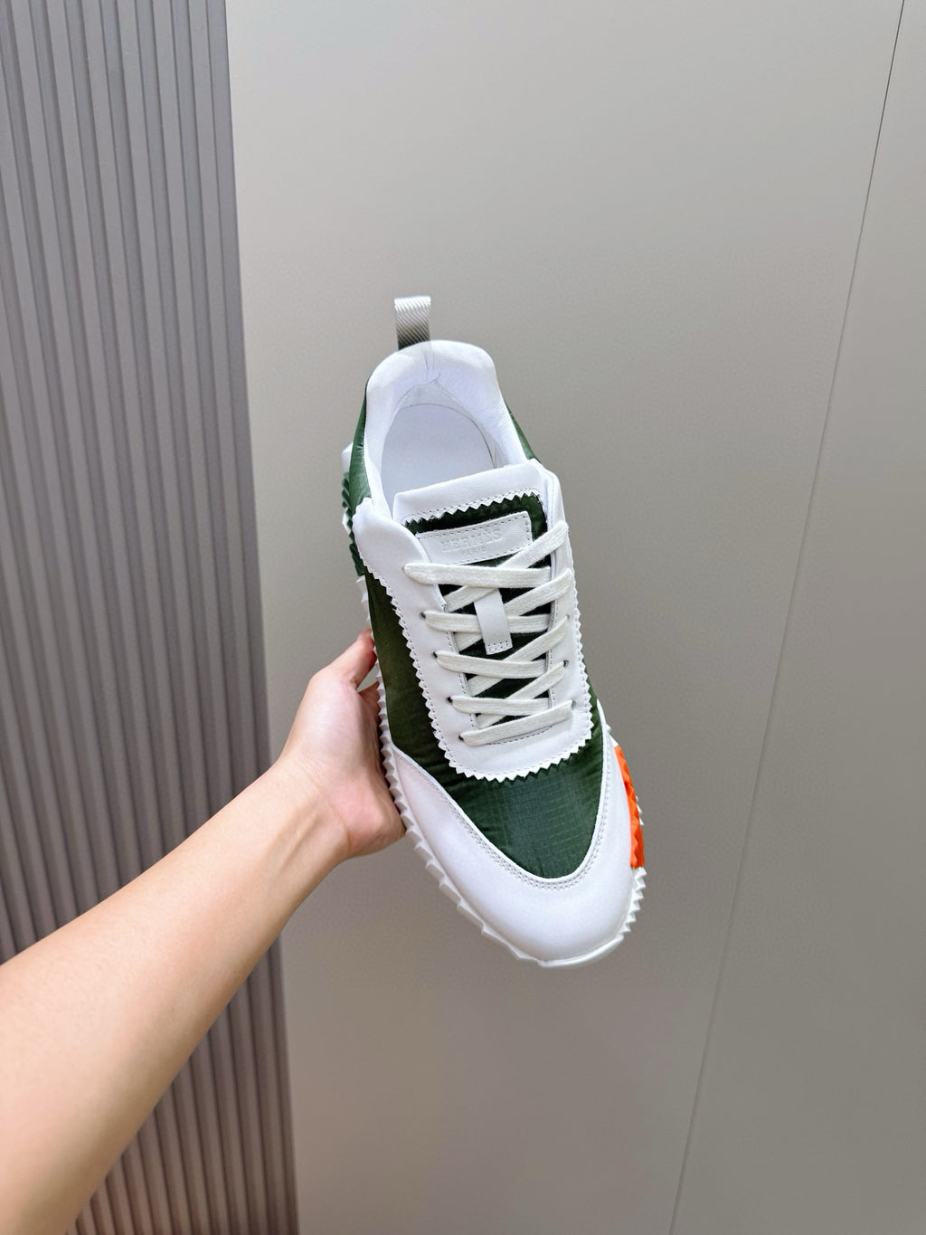 Hermes unisex sneaker held up, white laces on dark green suede-look upper