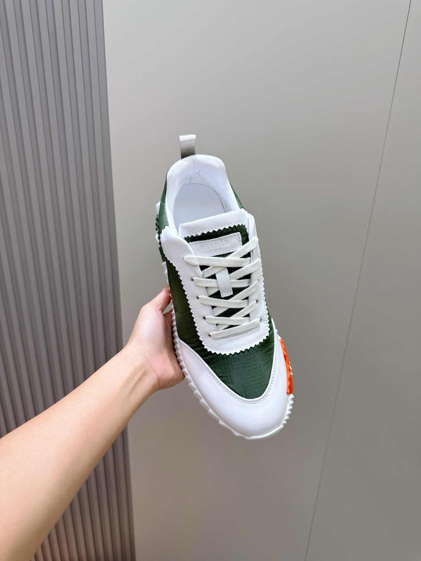 Hermes unisex sneaker held up, white laces on dark green suede-look upper