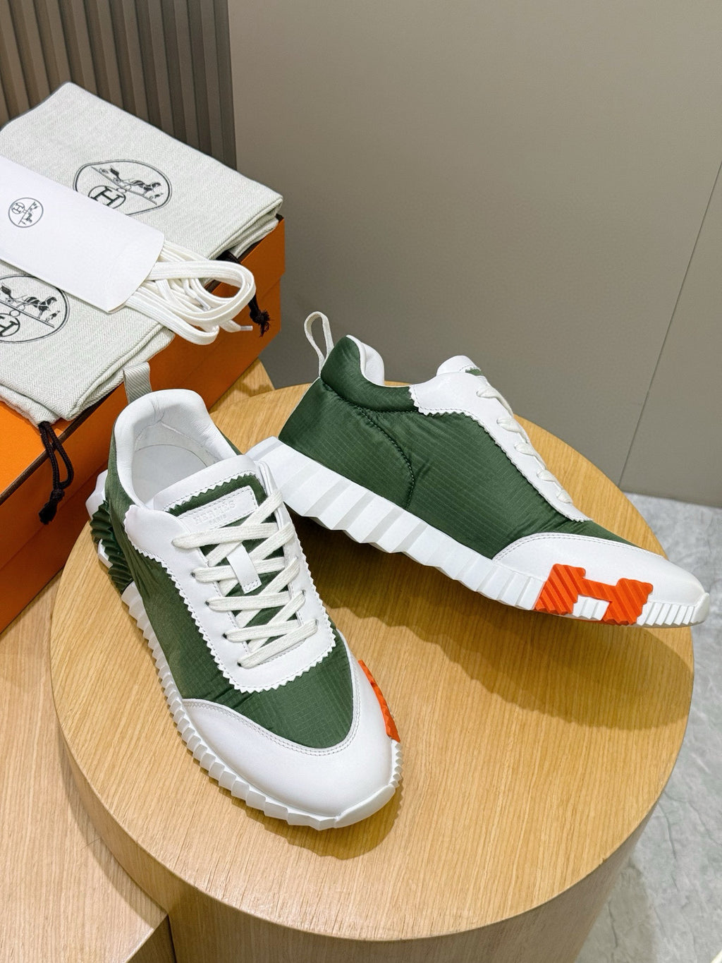 Hermes unisex sneakers on round display, white laces with dark green panels