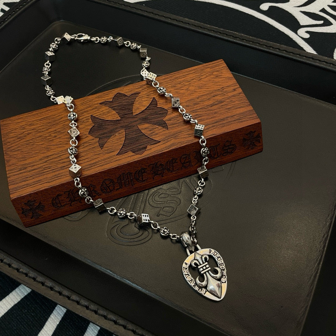 Silver-tone charm necklace on wooden box with heart pendant and floral emblem