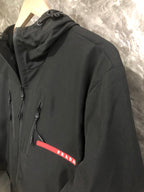 Black hooded long jacket with zip front and red Prada logo patch on chest