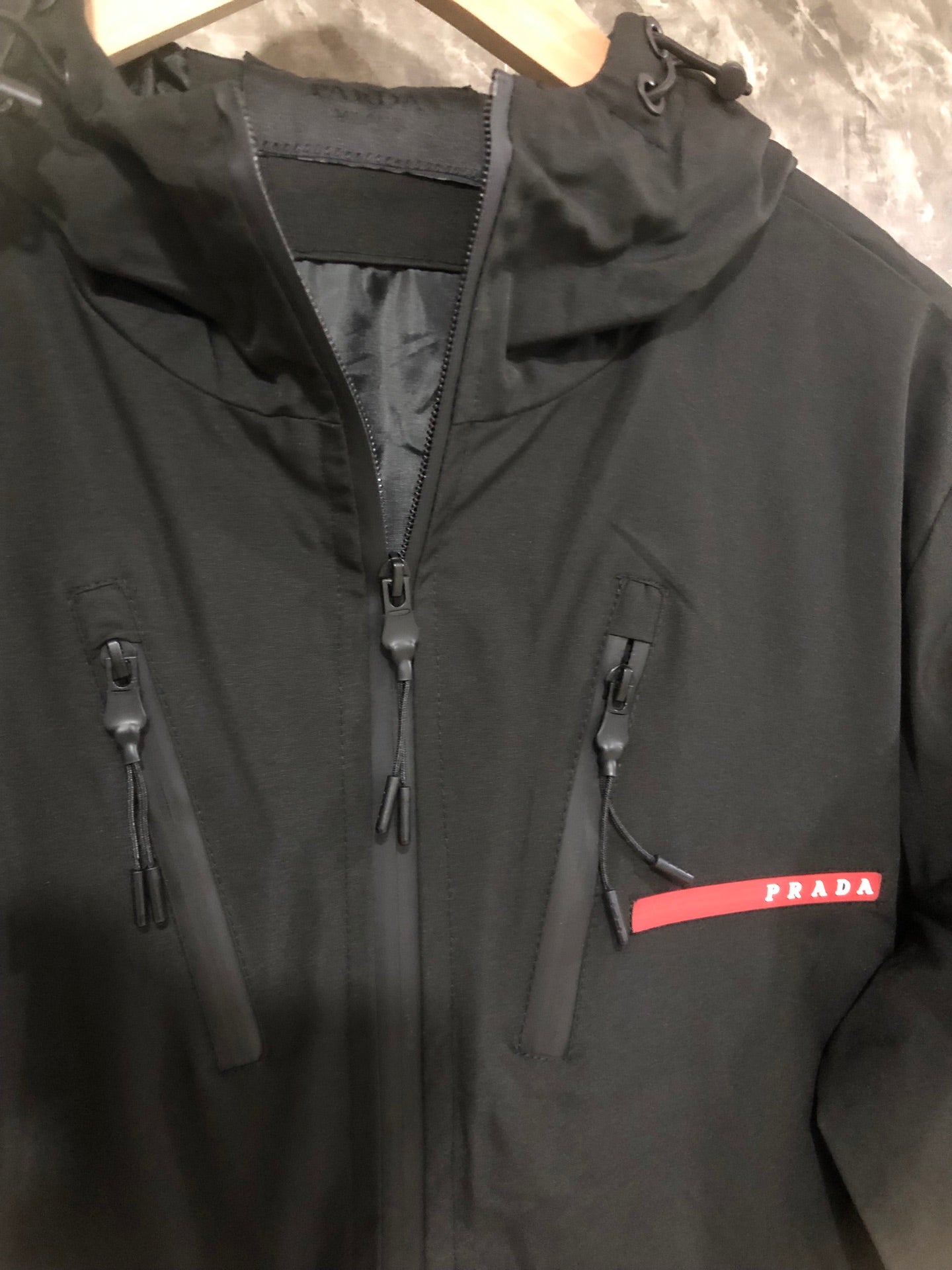Black hooded jacket close-up with zip front and red Prada logo patch