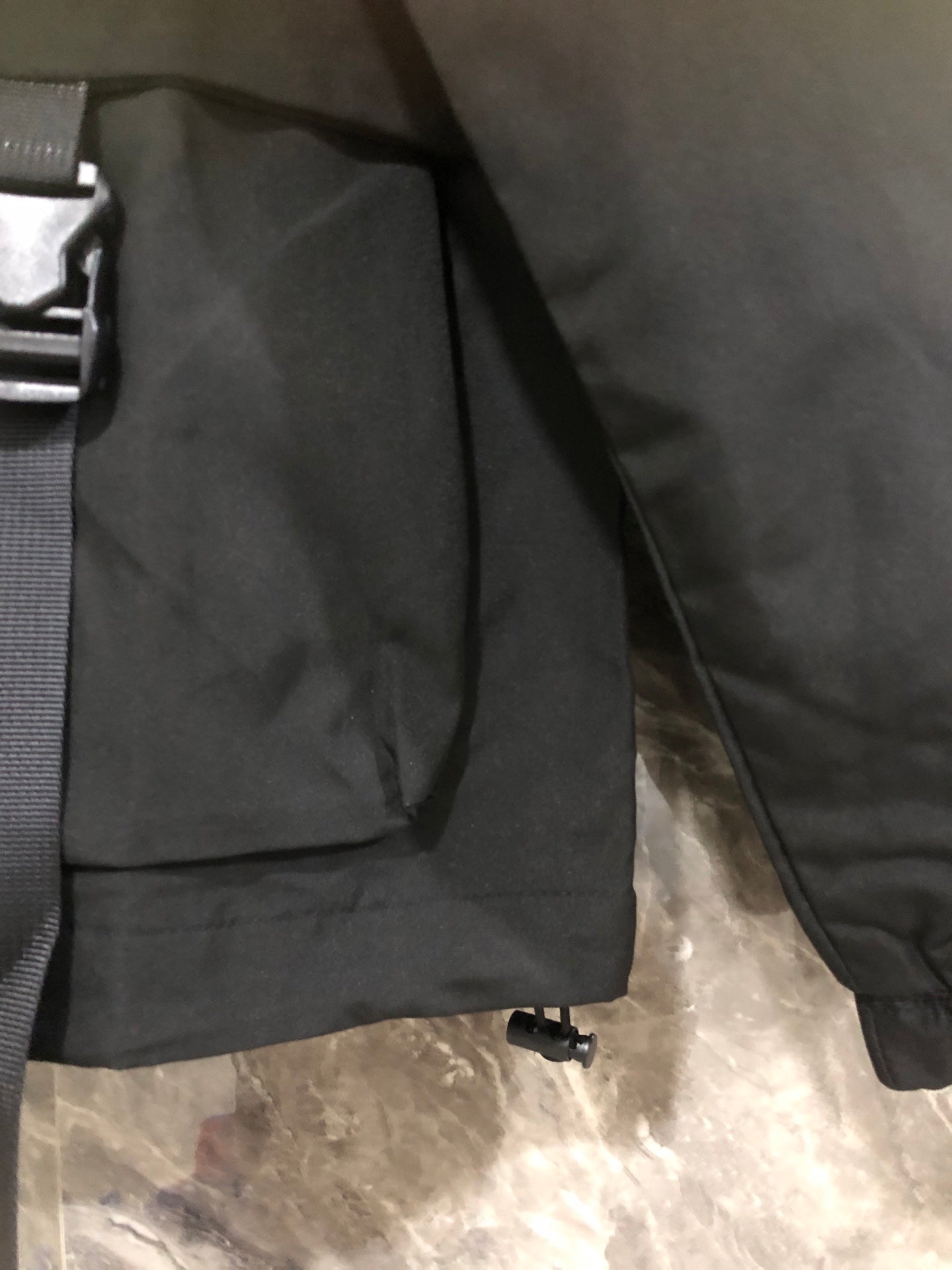 Black hooded jacket with front pocket flap and adjustable shoulder strap