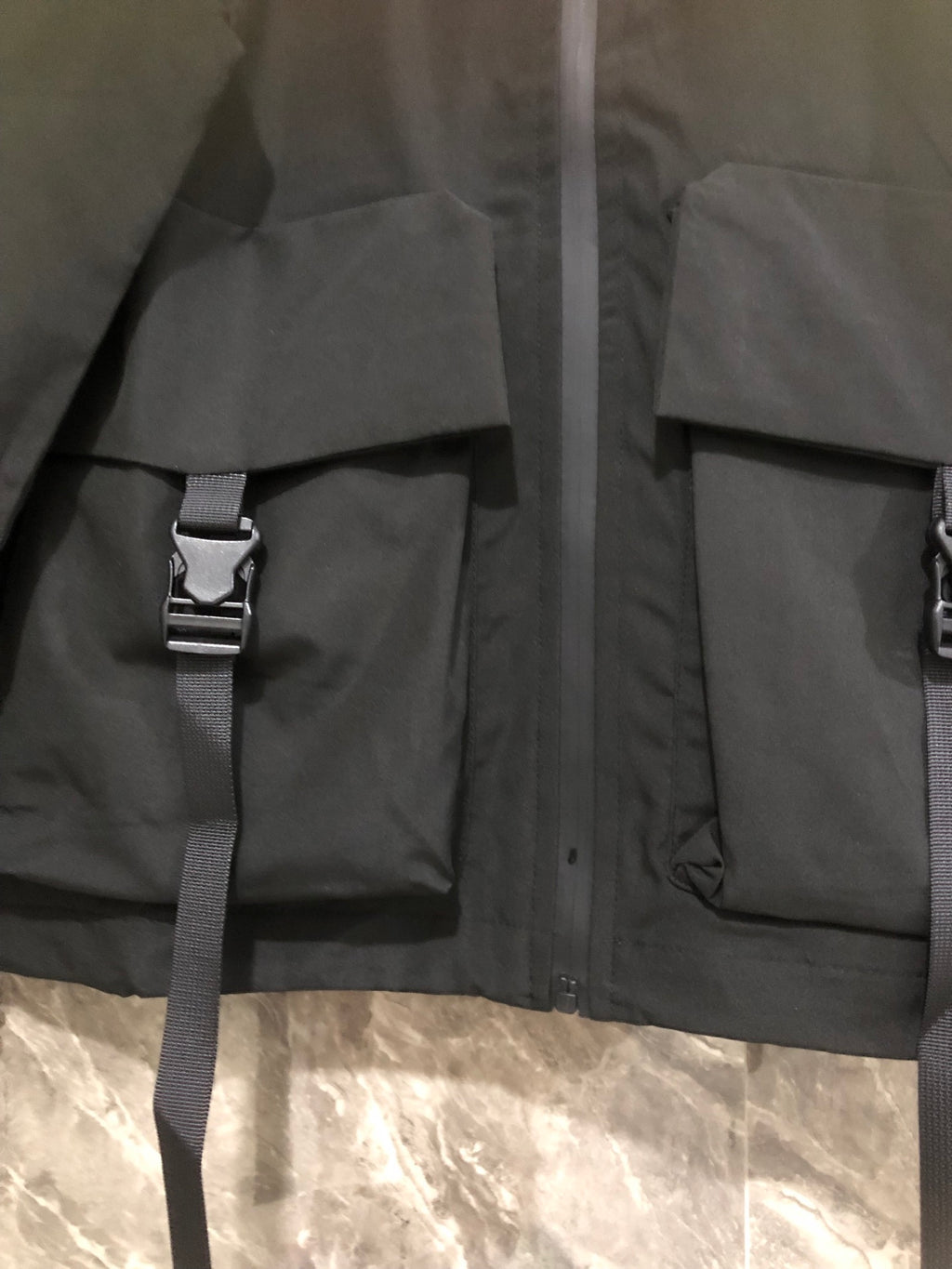 Black long jacket with hood, front utility pockets, and adjustable strap detail