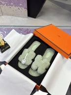 Mint green fluffy slide sandals with black outsole, laid in orange box