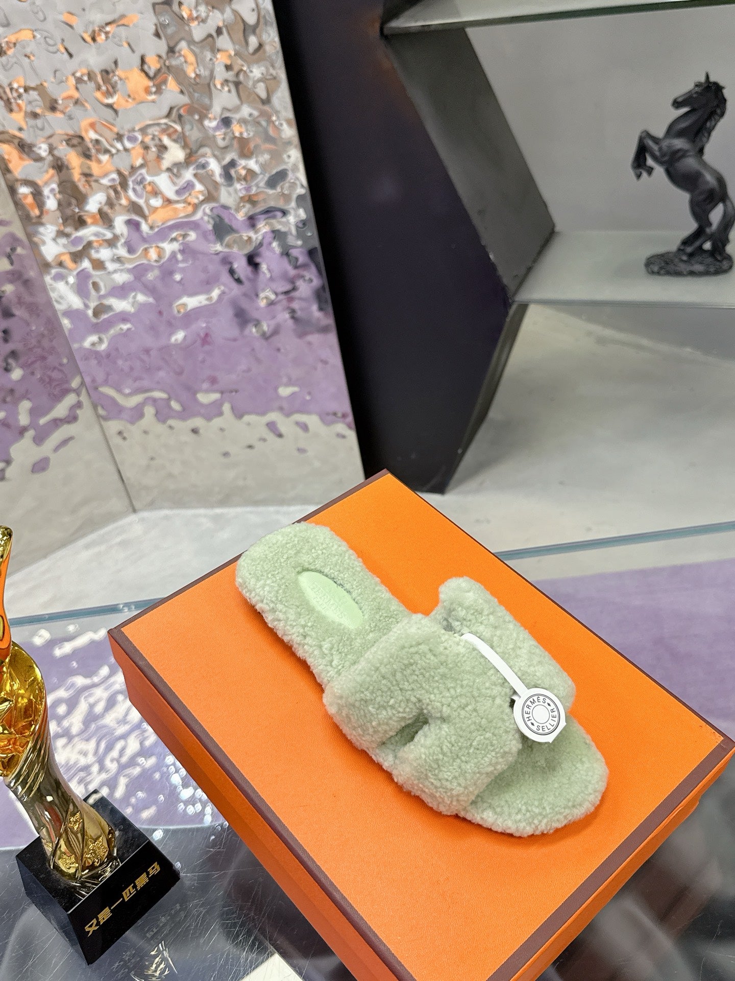 Mint green sherpa slide sandals with black sole, side view on orange box