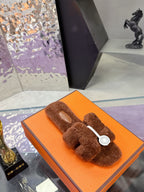 Brown plush slide sandals with white logo charm on wide crossover strap