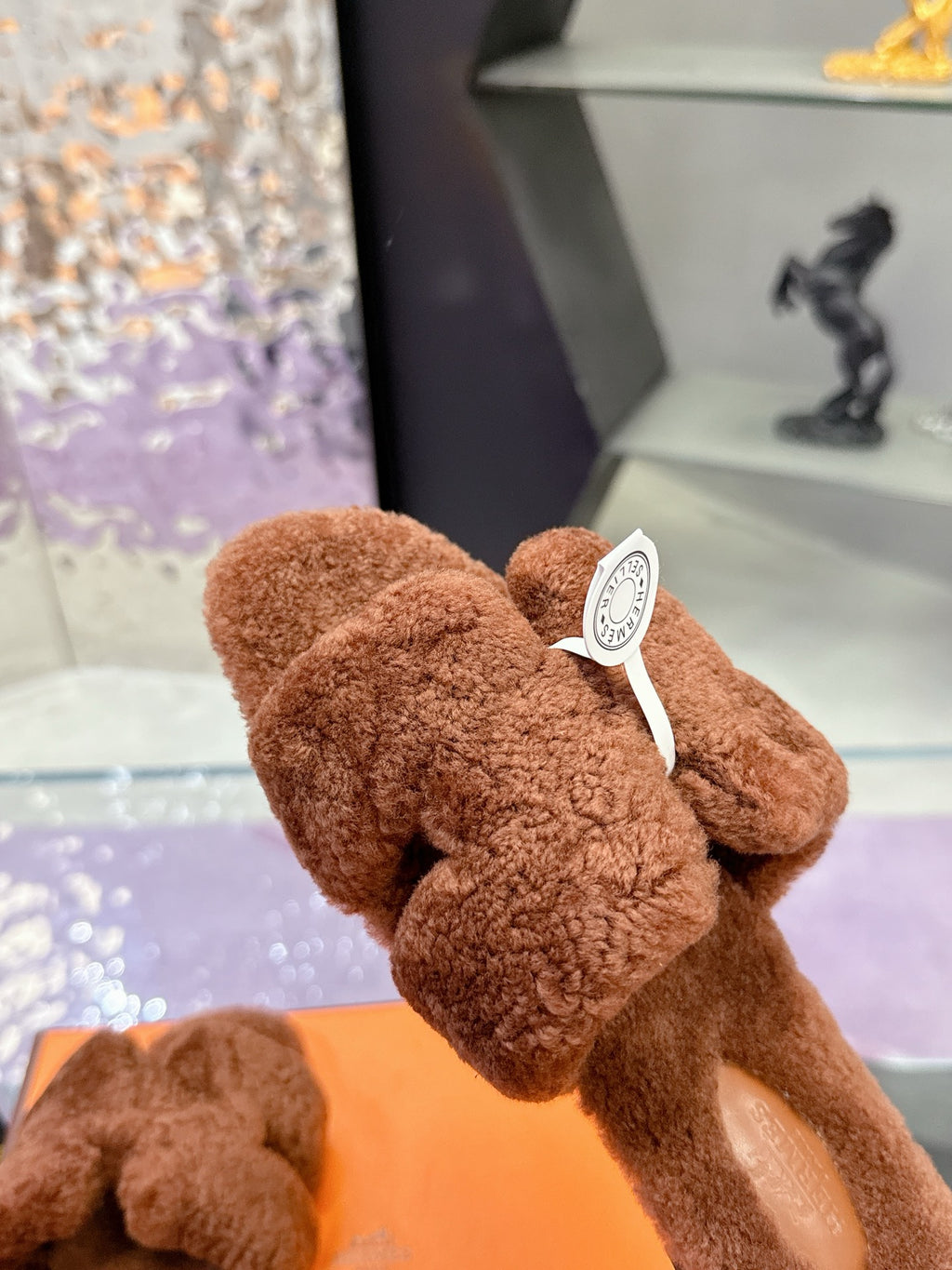 Brown teddy-fabric slide sandals, close-up of round white logo charm
