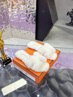 White plush slide sandals, front strap with round logo patch, shown in orange box