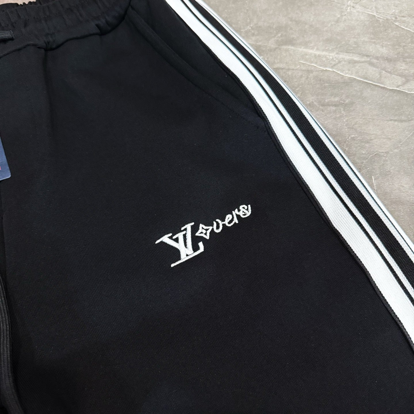 Black track pants with white and black side stripes and LV logo