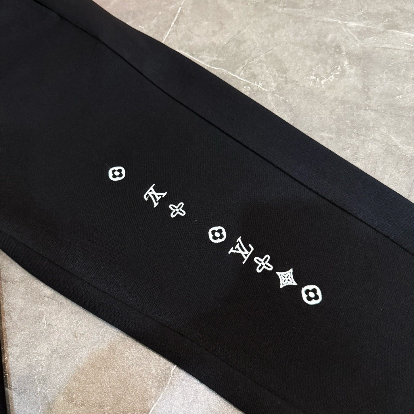 Louis Vuitton black pants detail with small LV and quatrefoil logos