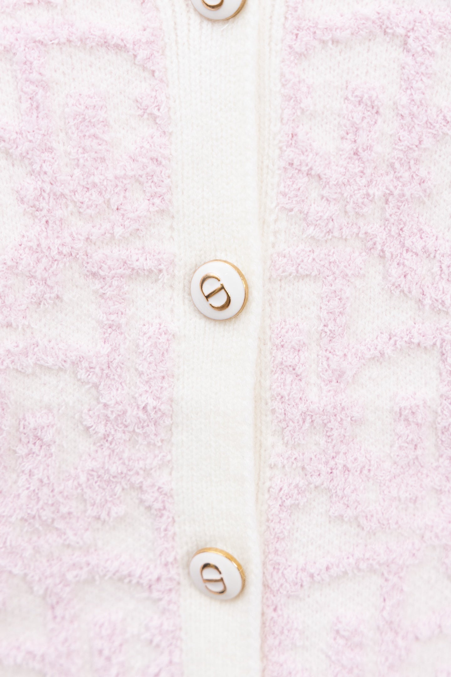 Cardigan button detail on pale pink textured knit with white placket and logo buttons