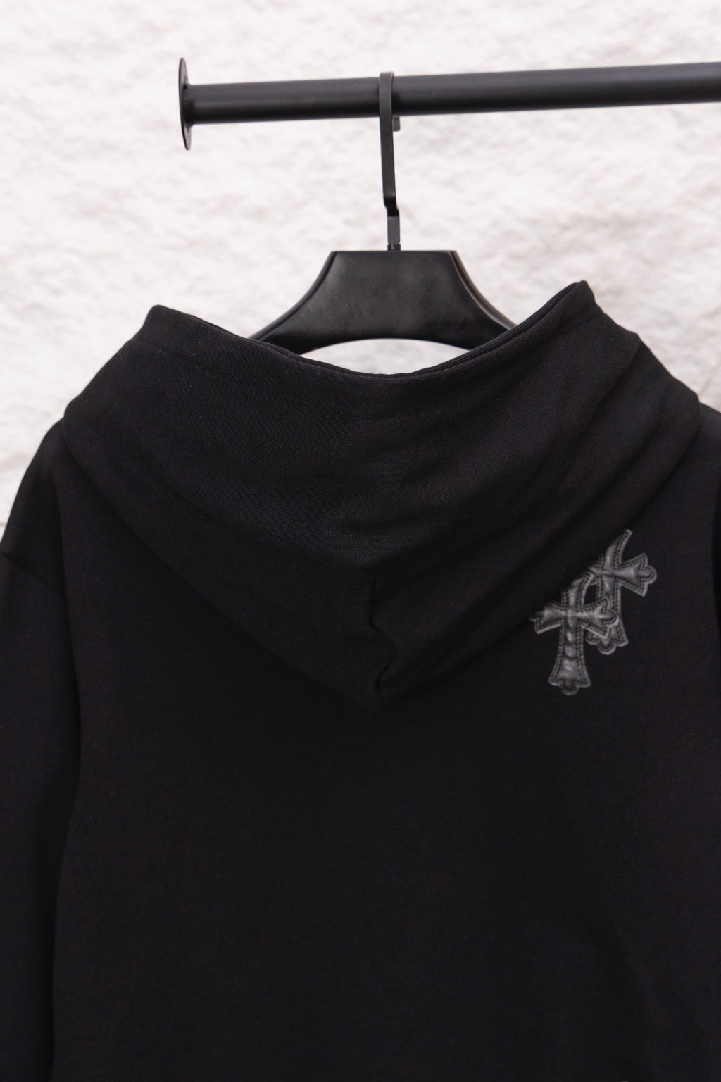 Black hoodie with hood and embroidered cross emblem on the upper sleeve