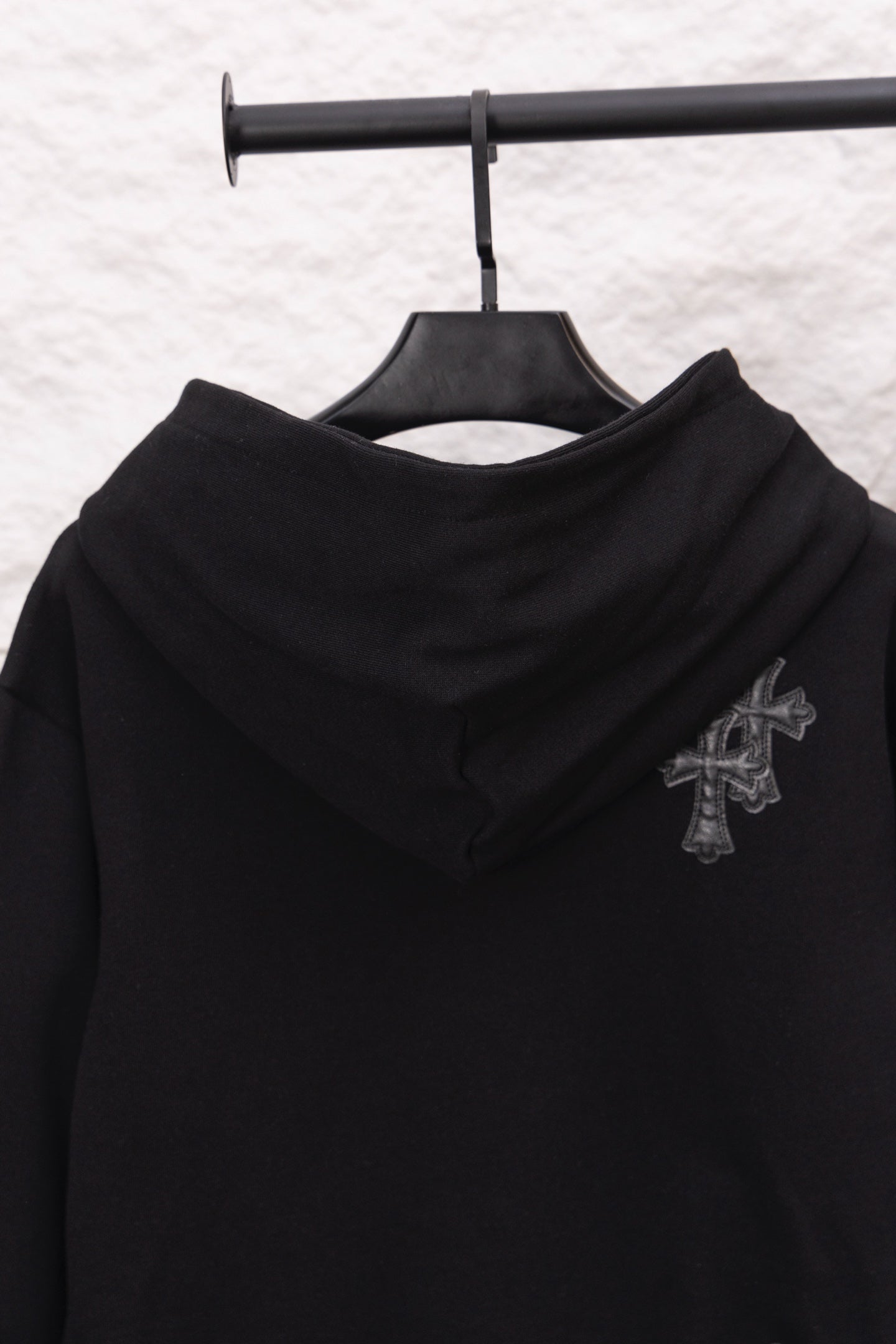 Black hoodie with hood and embroidered cross emblem on the upper sleeve