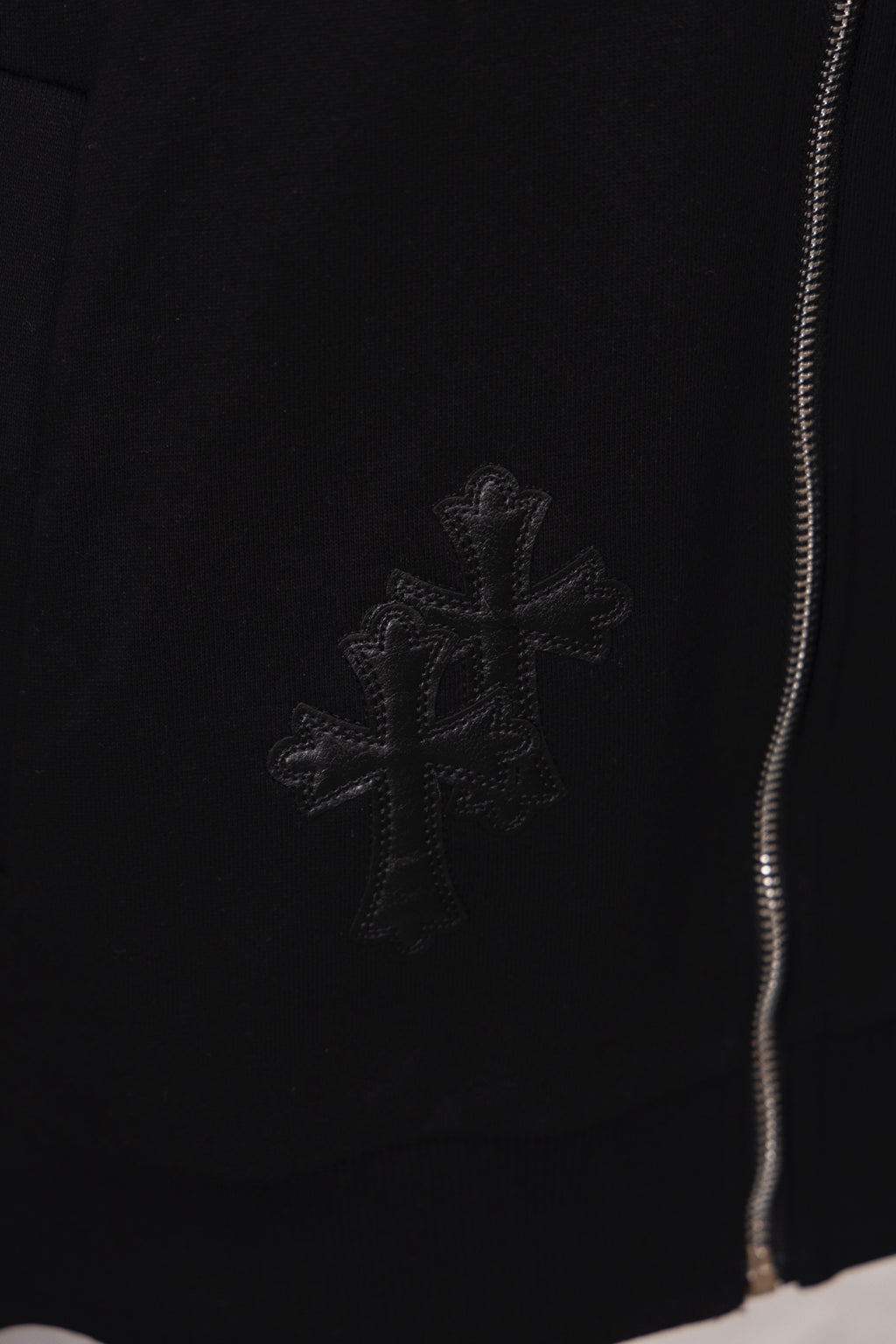 Black hoodie with small cross emblem embroidery near the hem and zipper edge
