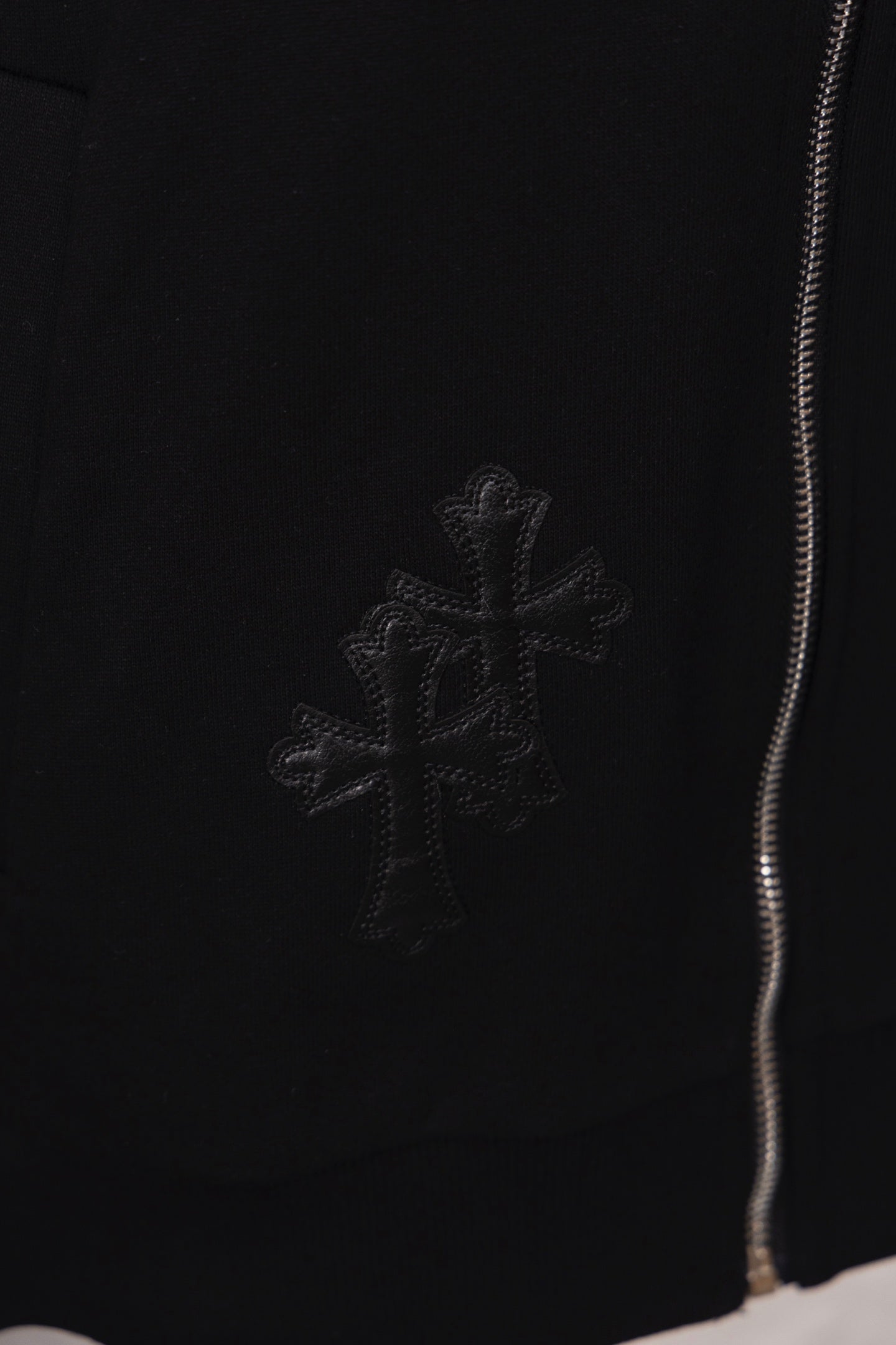 Black hoodie with small cross emblem embroidery near the hem and zipper edge
