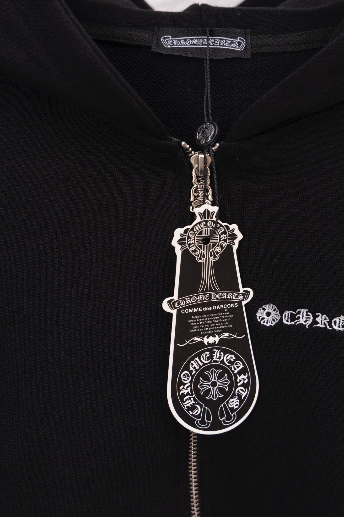 Close-up of black hoodie zipper and hood pull with circular metal crest charm