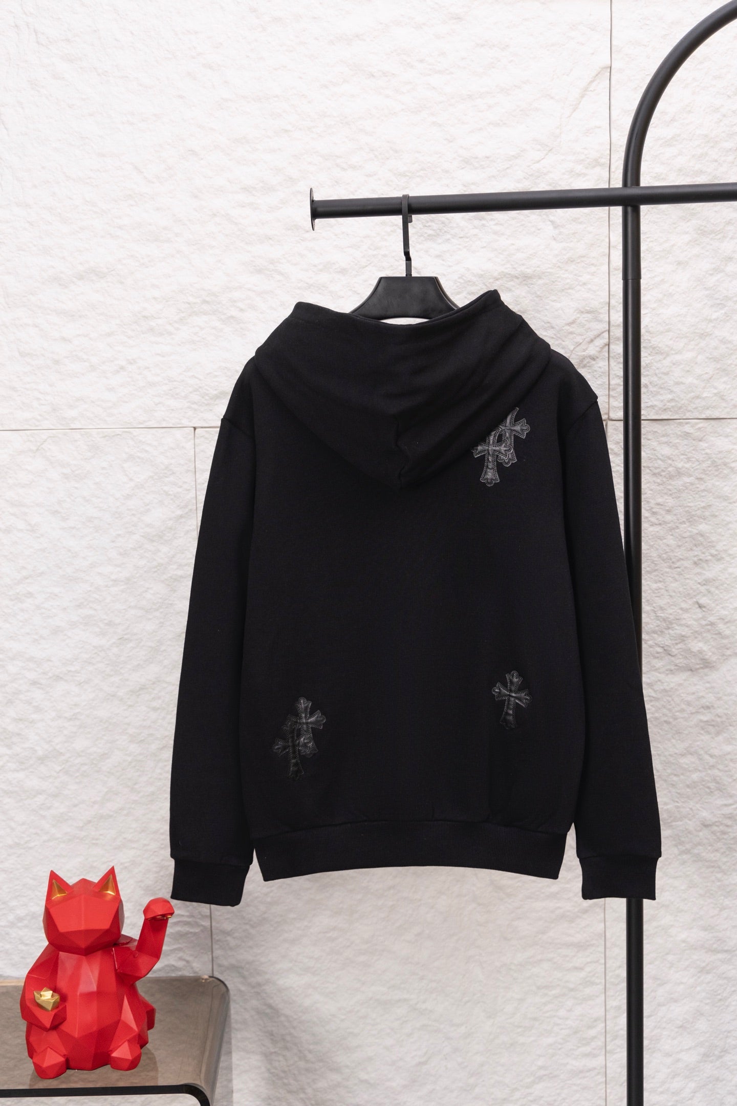 Black pullover hoodie with hood and front zipper; small cross-style embroidery details