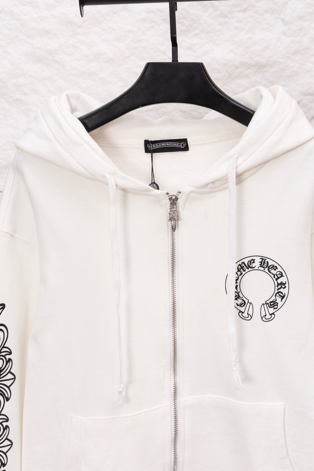 White zip-up hoodie close-up with hood, front zipper, and chest logo patch