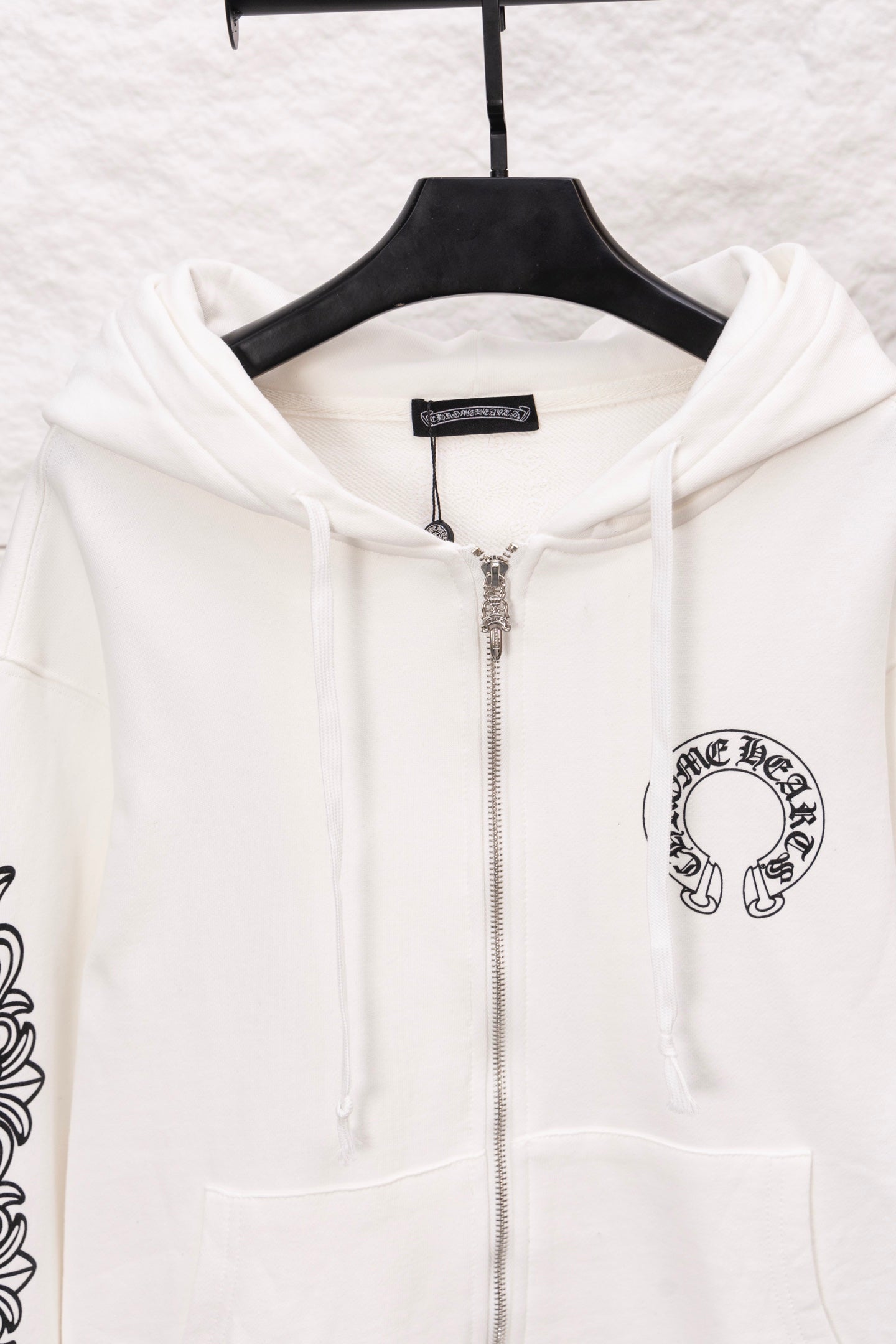 White zip-up hoodie close-up with hood, front zipper, and chest logo patch