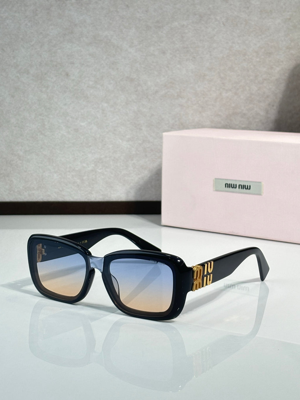 Black cat-eye sunglasses with blue lenses and gold temple logo detail