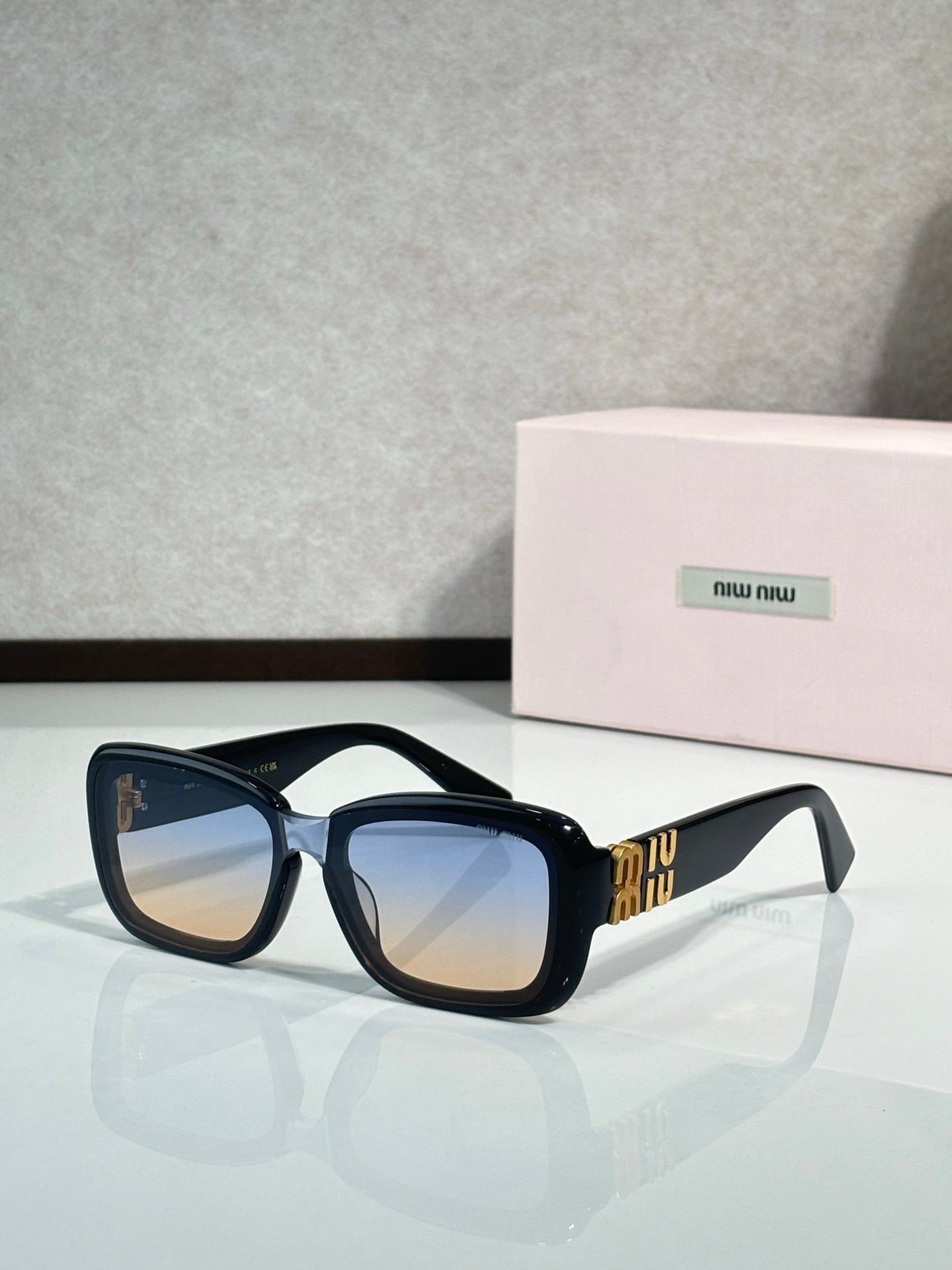 Black cat-eye sunglasses with blue lenses and gold temple logo detail