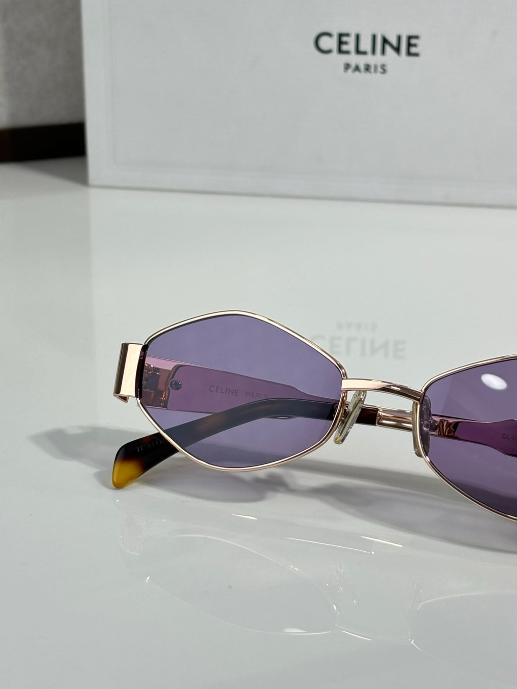 Purple-tinted oval sunglasses with gold frame and dark lenses