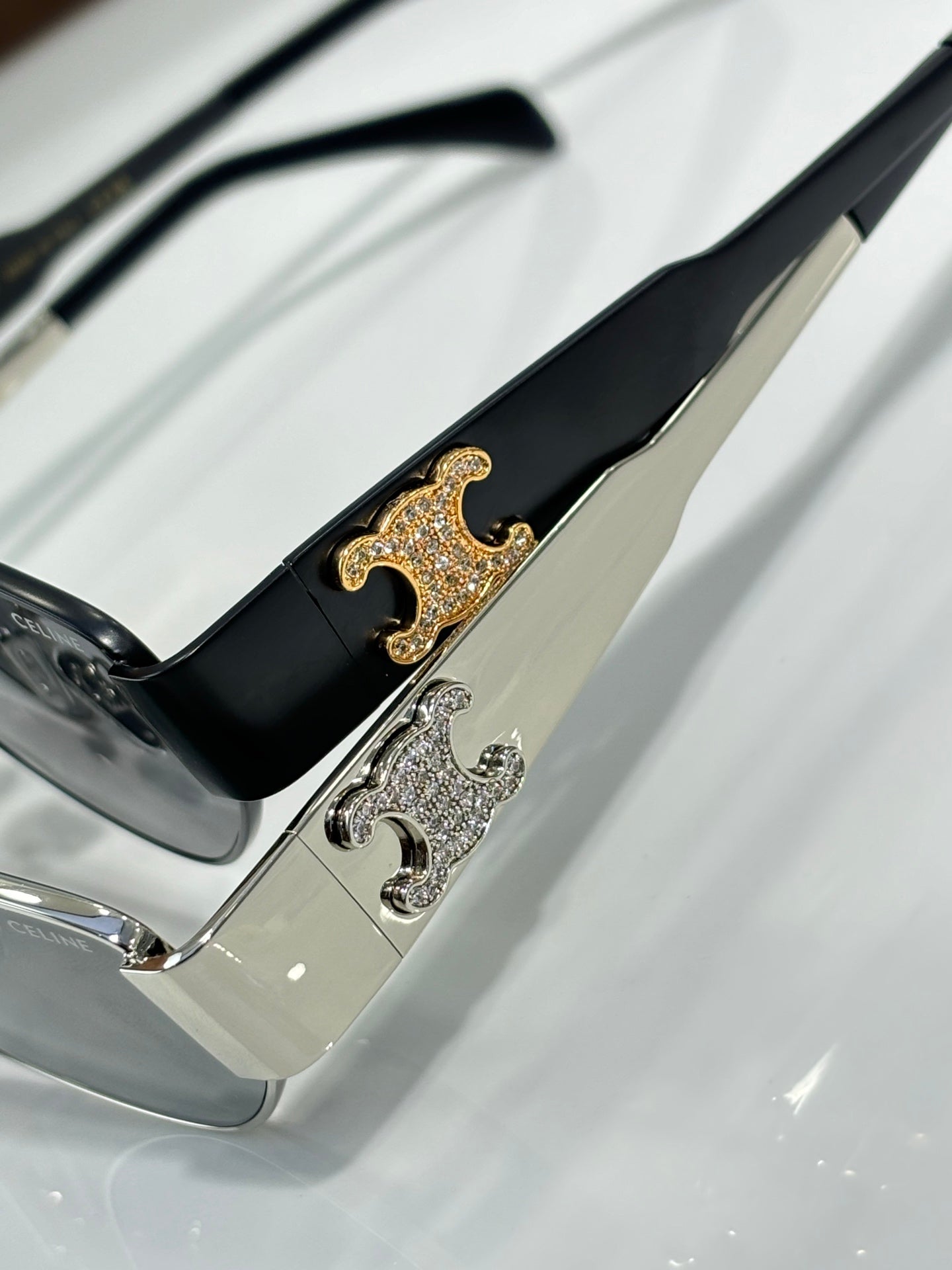 Black sunglasses temple close-up with gold and silver logo detail