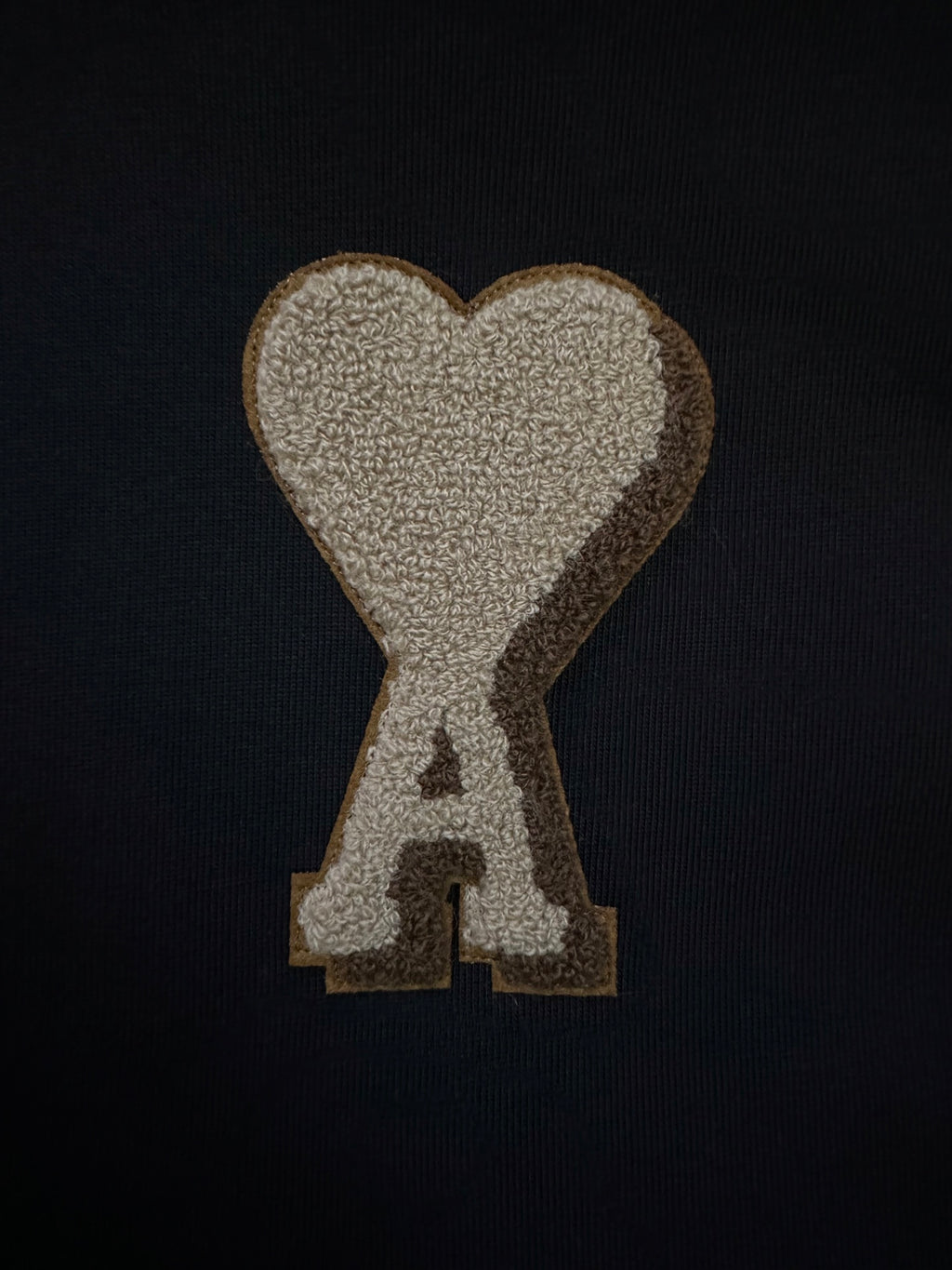 Heart-shaped "A" appliqué patch in beige/gold on black fabric